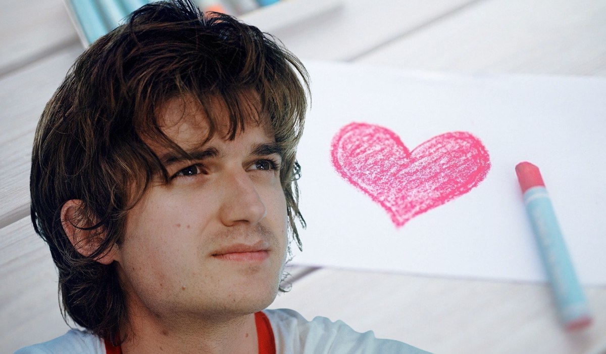 Portrait of Joe Keery beside a drawing of a pink heart, symbolizing public interest in his personal life, relationships, and career
