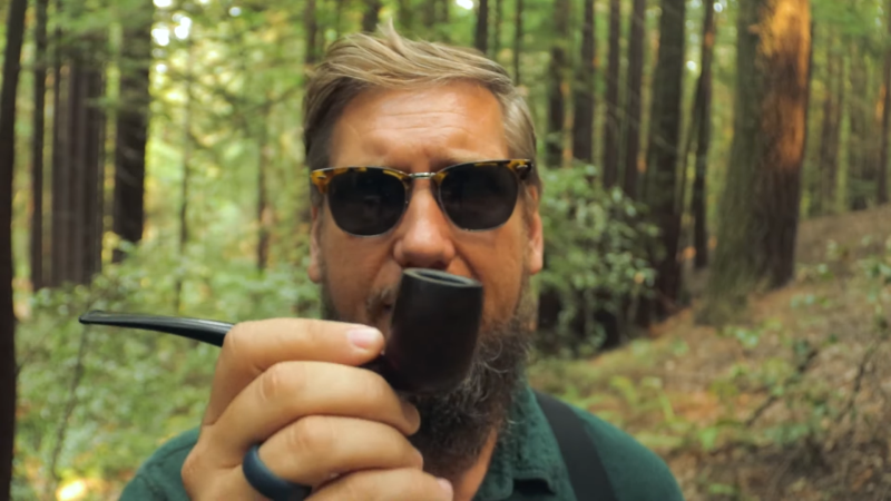 Man in forest holding a smoking pipe close to the camera. 