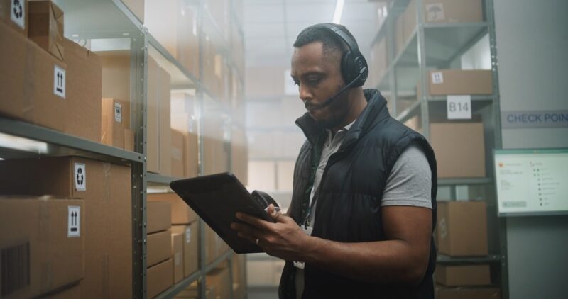 Warehouse worker checking inventory on a tablet, showing hidden fees contributing to business overhead in logistics