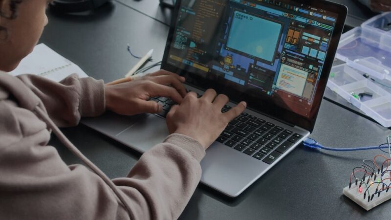 Person coding on a laptop surrounded by electronics, illustrating hidden business overhead from overlooked SaaS costs