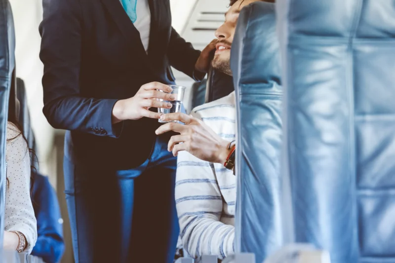 The steward gives a passenger a glass of water on the plane
