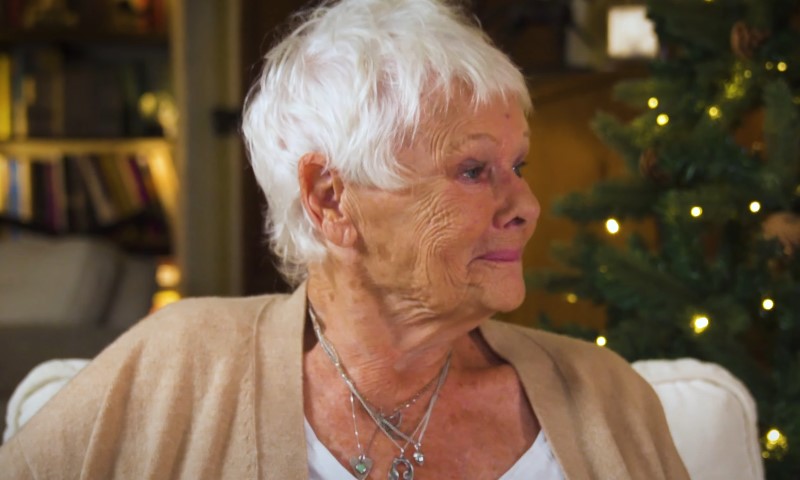 Judi Dench sitting in front of a decorated Christmas tree