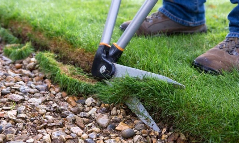 Person trims grass edge along a stone path with pruning shears