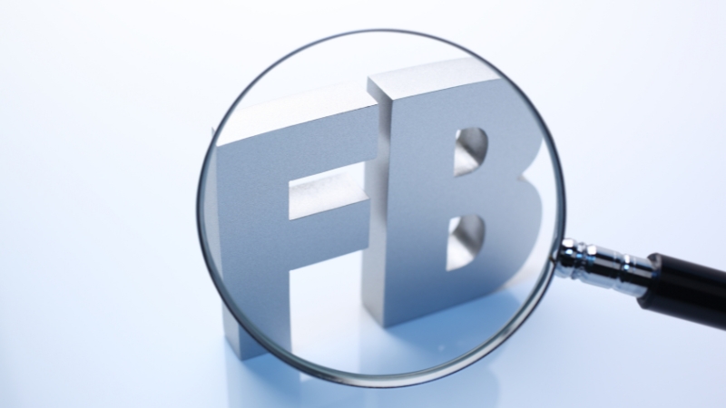 Magnifying glass over Facebook logo symbolizing repeated Community Standards violations on Facebook