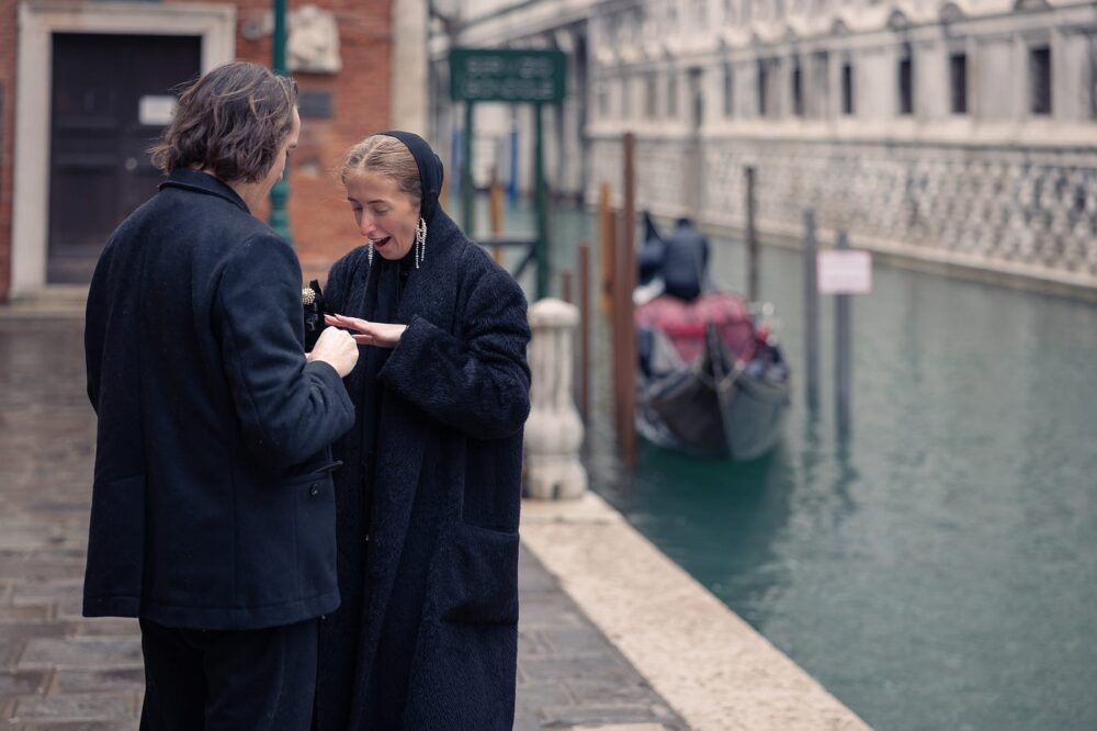 A person places a ring on their partner’s finger beside a quiet canal in Venice.