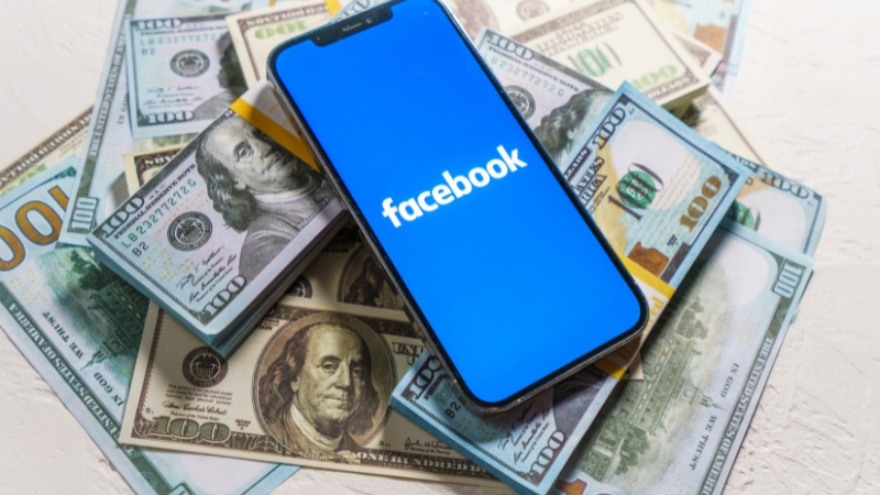 Smartphone with the Facebook app on the screen placed on U.S. dollar bills