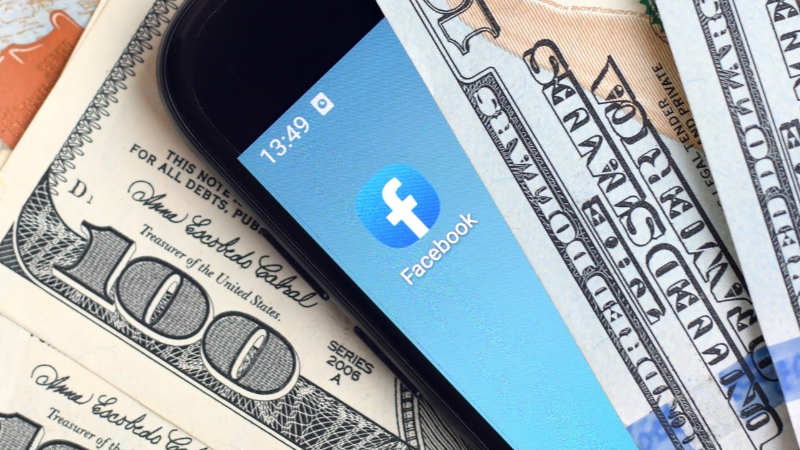 Smartphone with the Facebook app on a screen placed on dollar bills, illustrating Facebook payouts for creators
