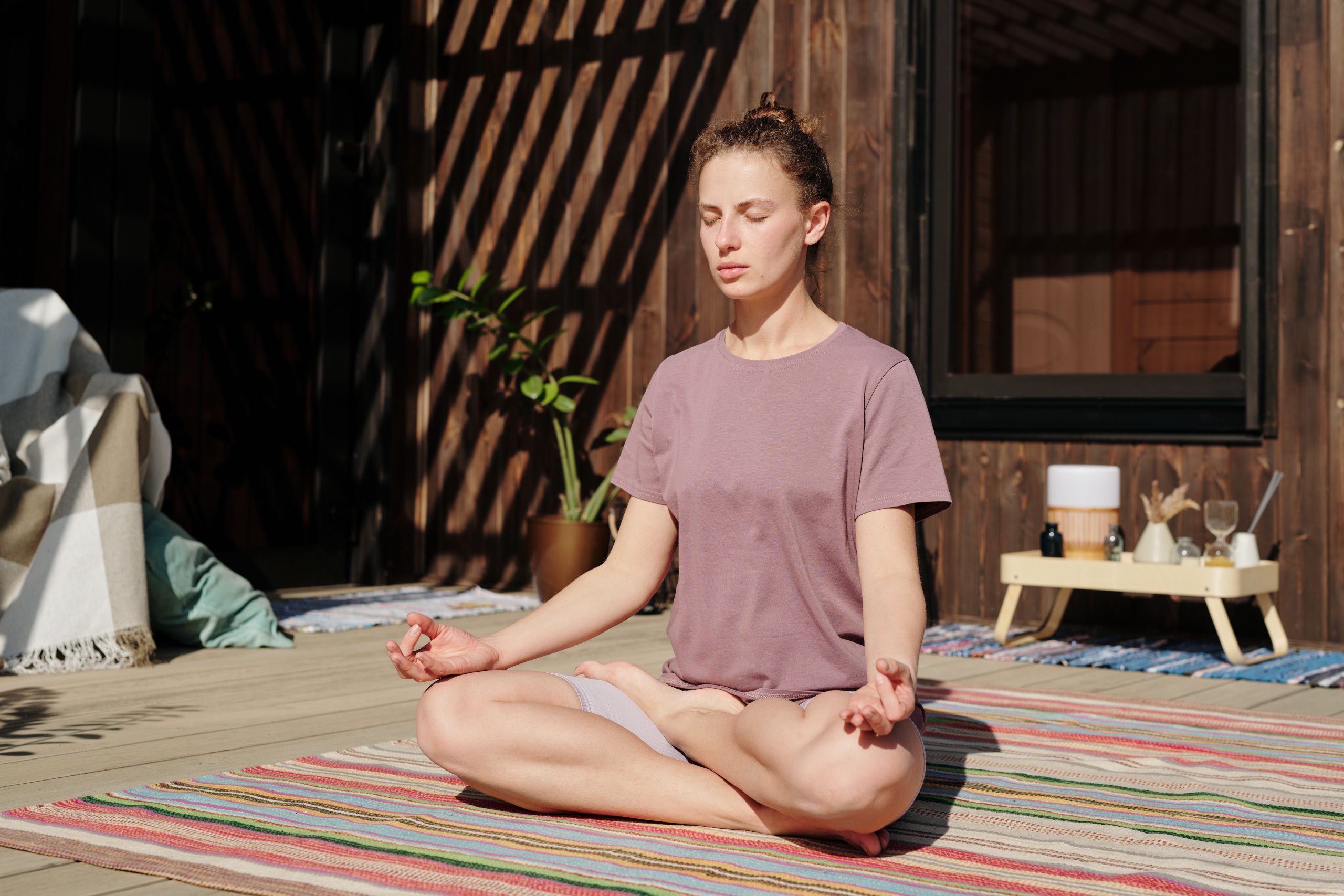 Woman practicing meditation in lotus pose on a sunny outdoor deck, ideal for beginners exploring meditation