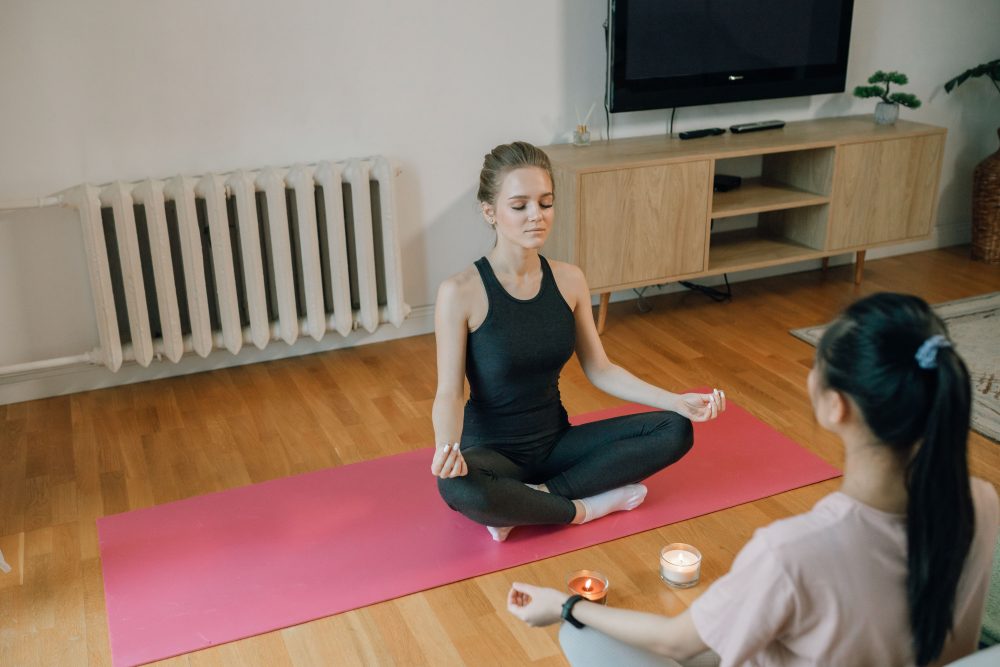 Two beginners meditating together on yoga mats indoors, practicing mindfulness