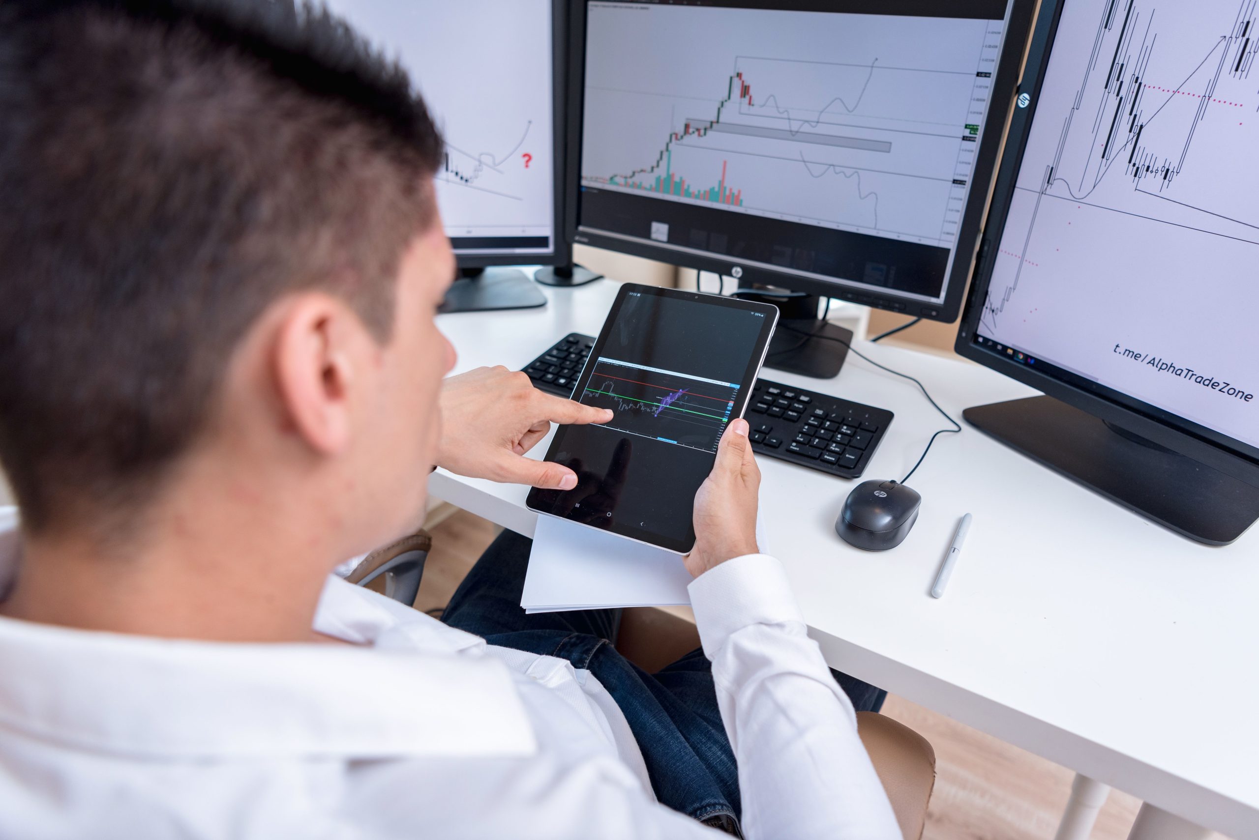 Investor analyzing cryptocurrency charts across multiple monitors and a tablet