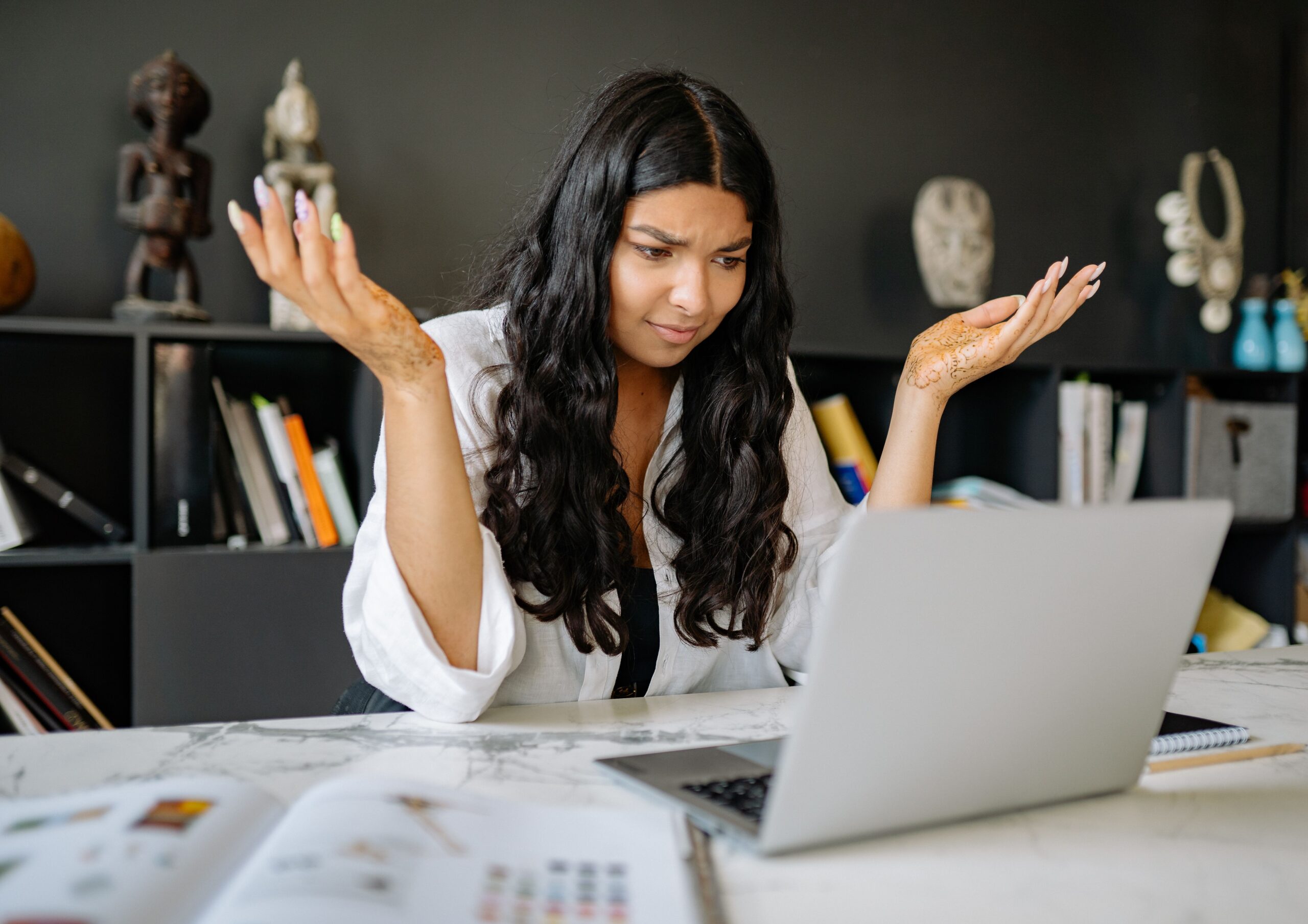 Frustrated woman at office desk staring at laptop screen in disbelief