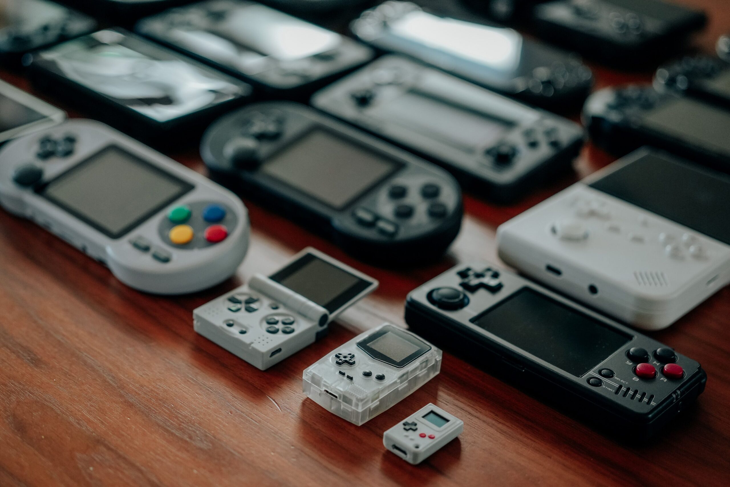Collection of diverse retro handheld gaming consoles on a wooden surface, showcasing classic designs