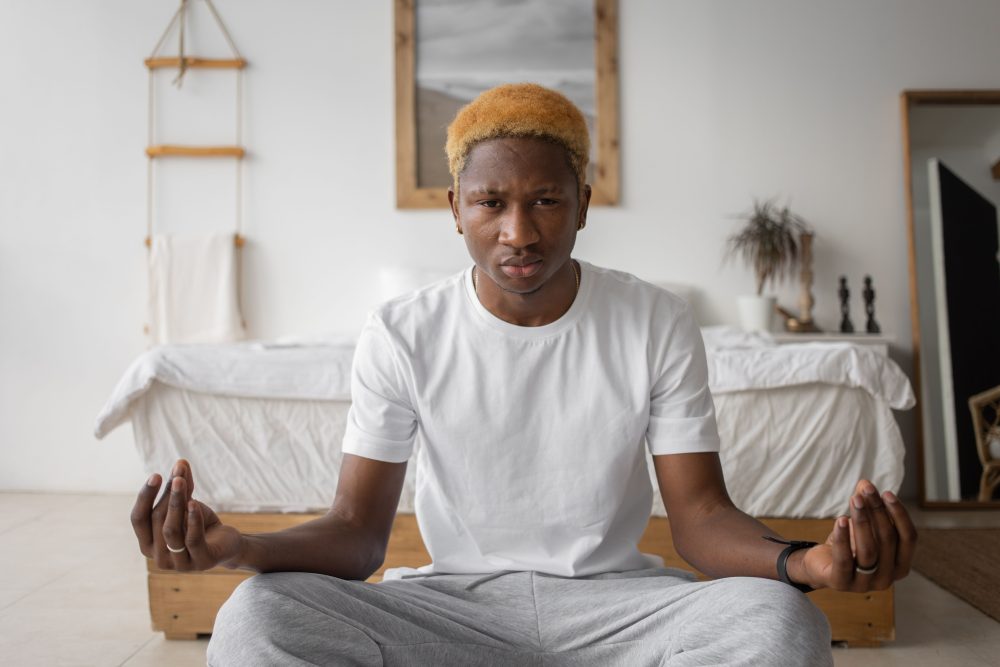 Young man meditating quietly alone in a serene bedroom, practicing mindfulness