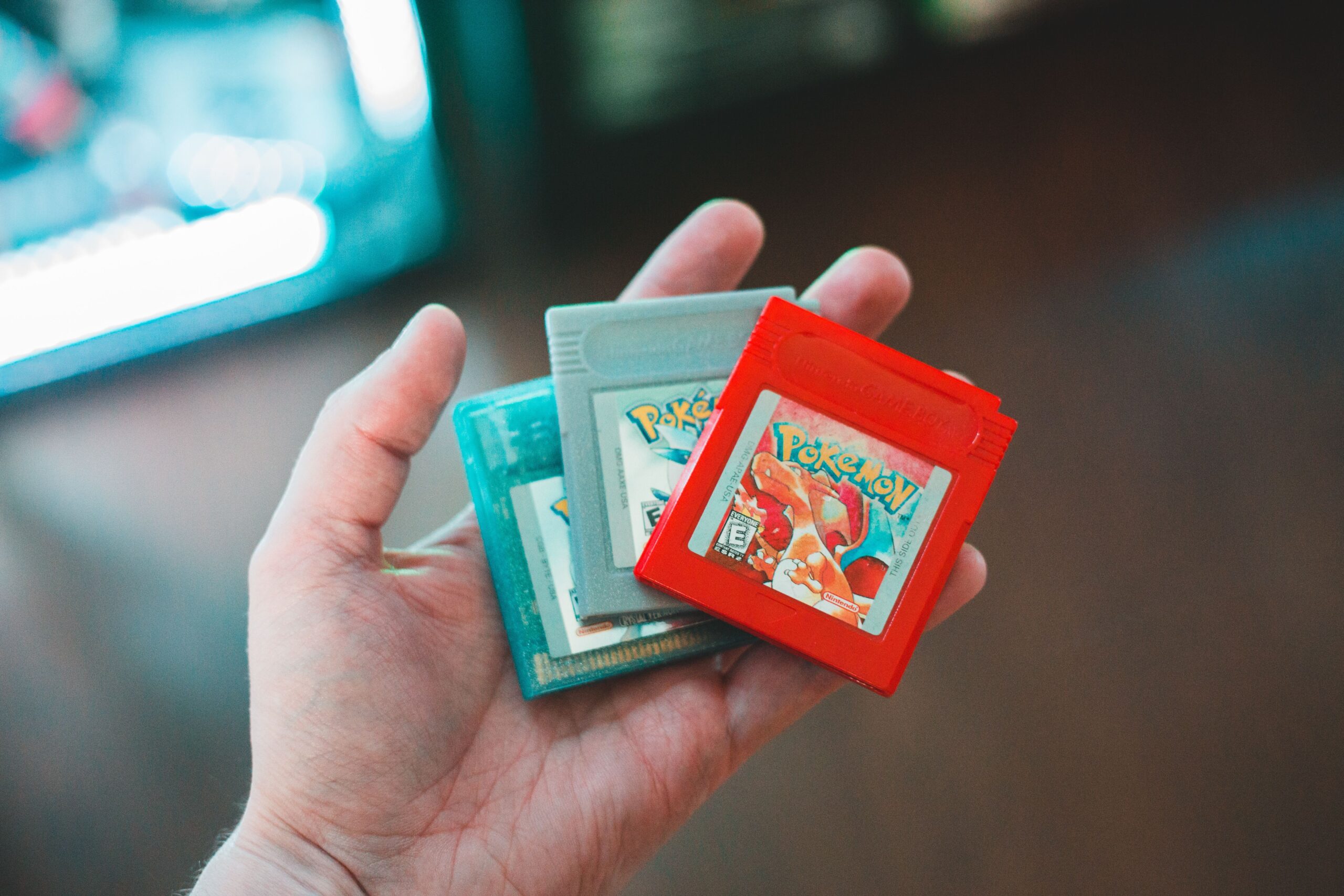 Hand holding vintage Pokemon game cartridges, showcasing nostalgic handheld gaming