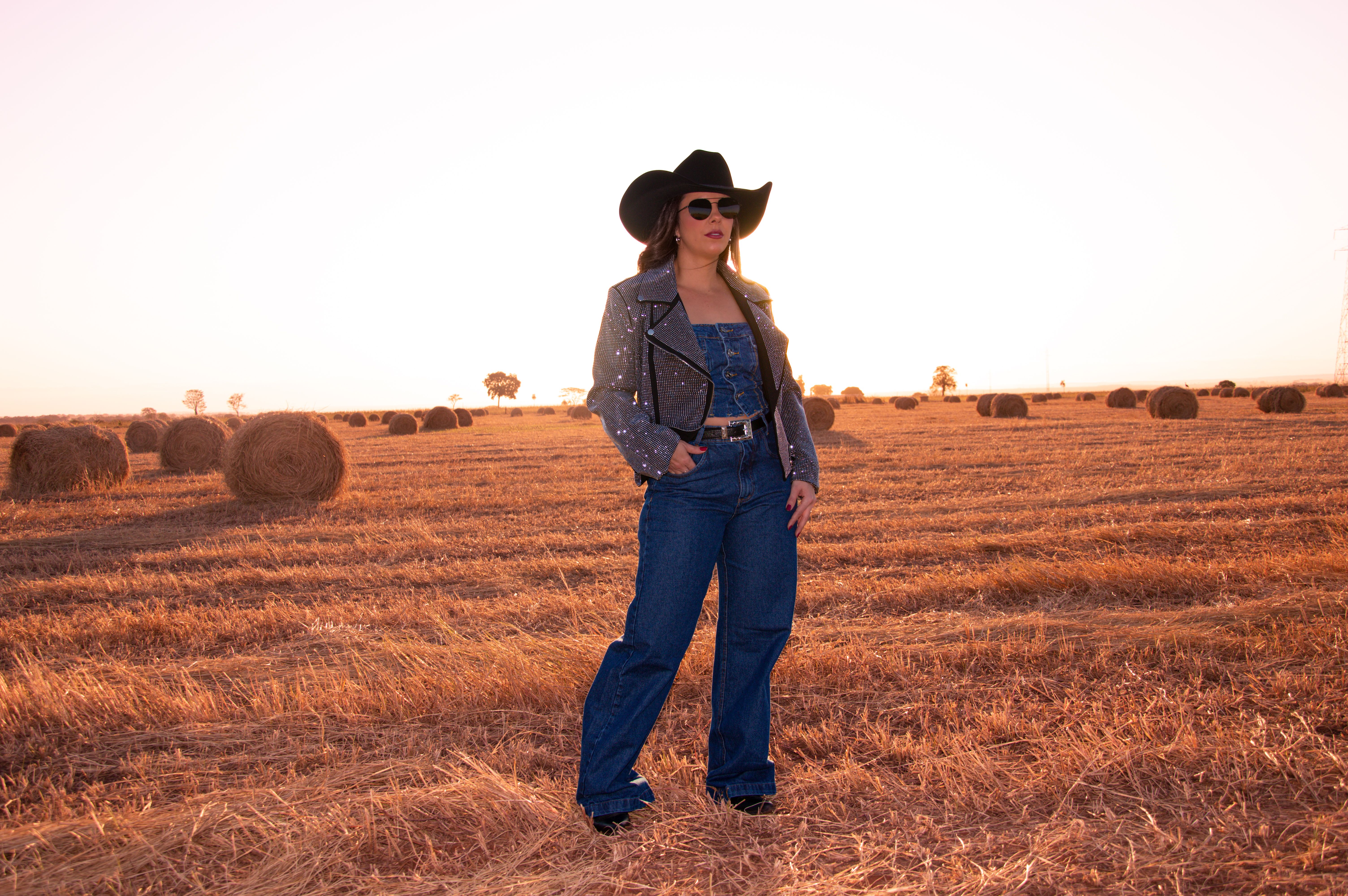Fashionable cowgirl standing in a hayfield at sunset embodying rustic elegance