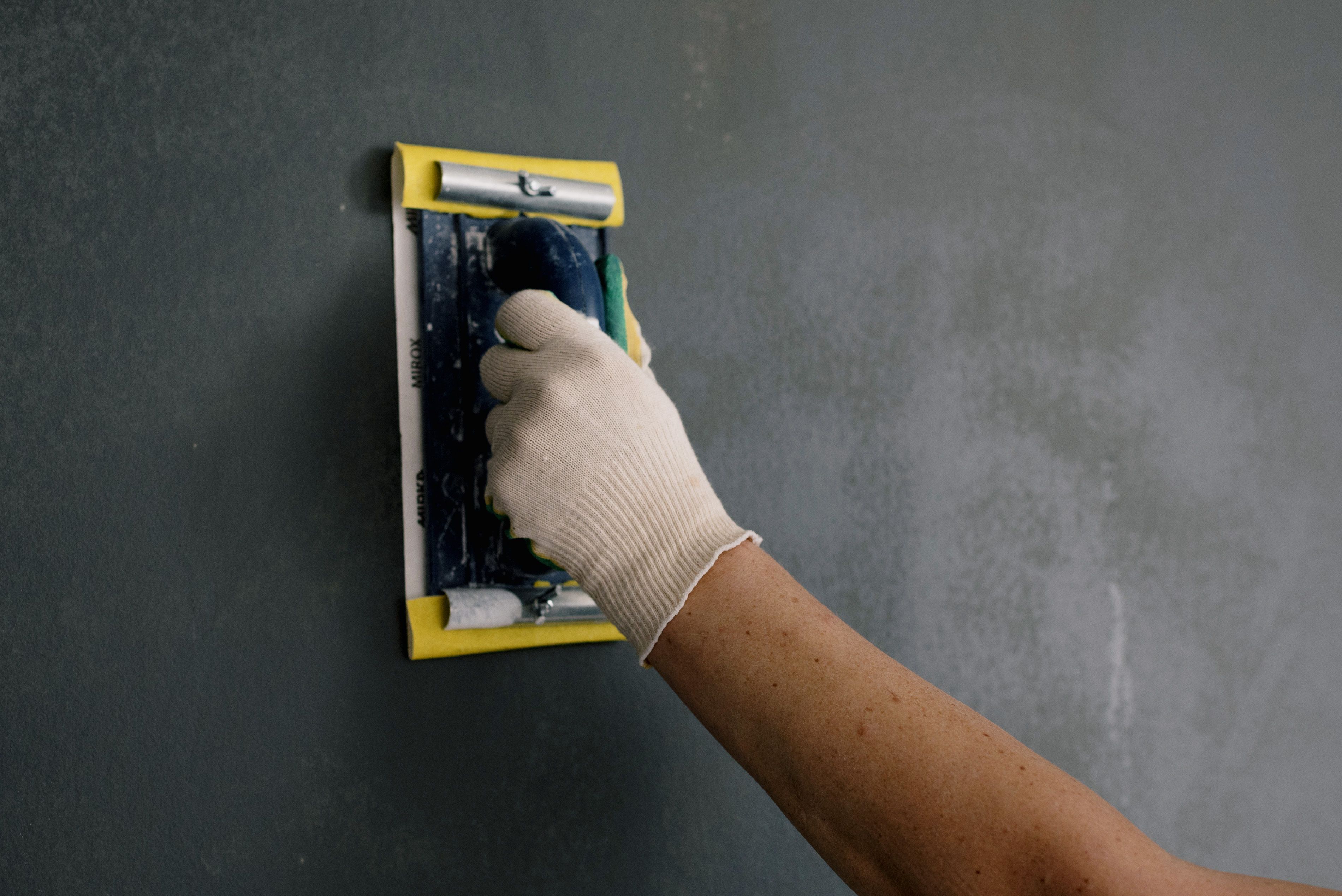 Person wearing gloves using a scraper to patch and renovate a damaged wall