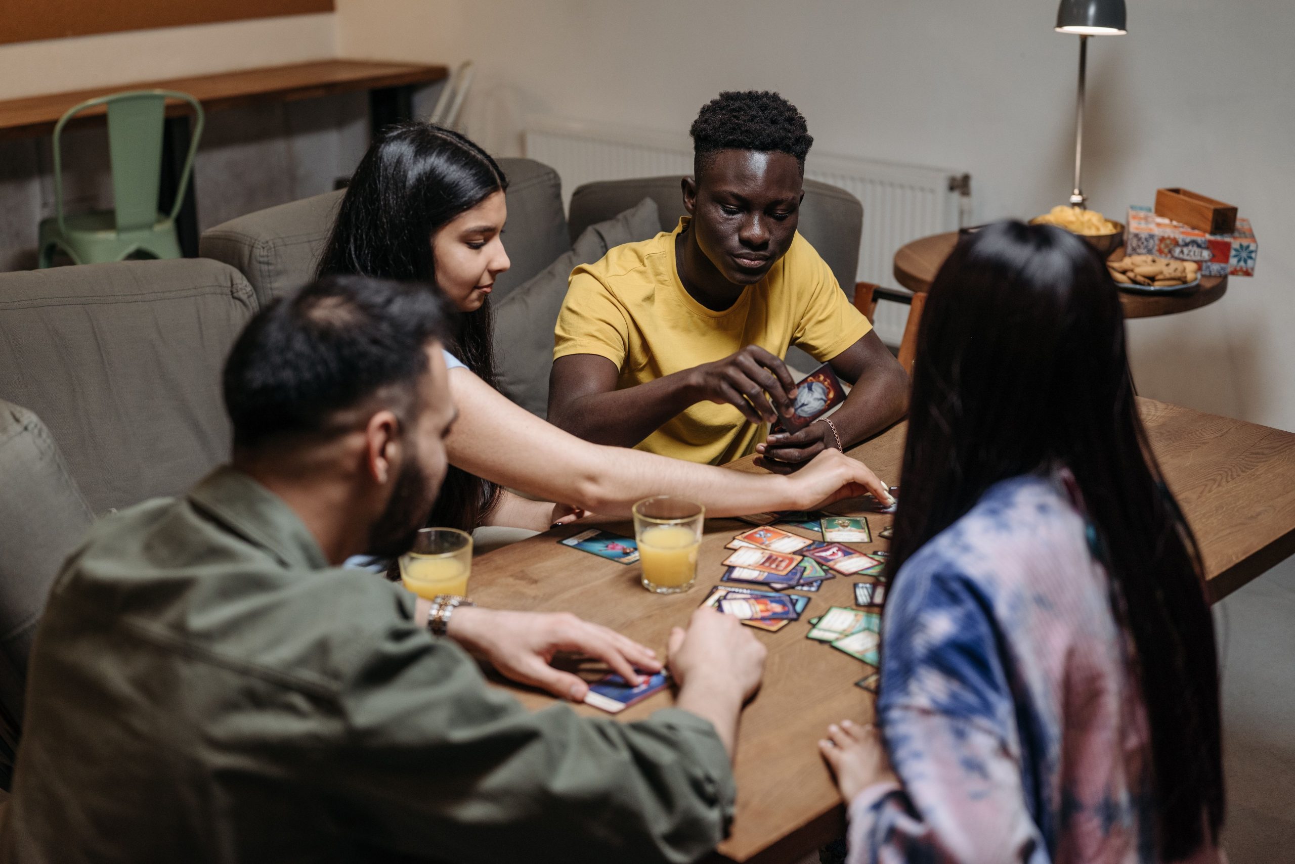 A diverse group of friends playing a strategic card game while enjoying drinks indoors.