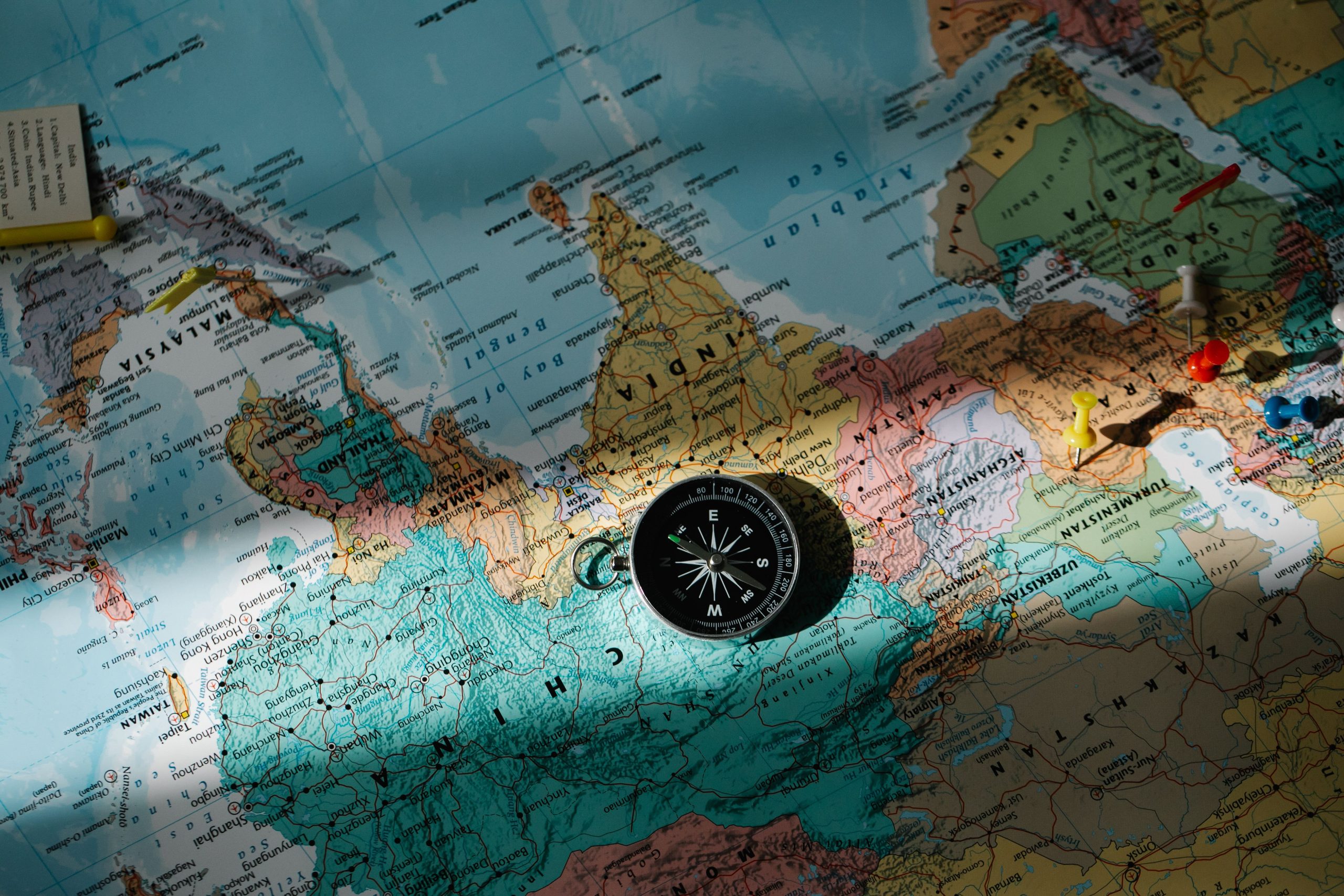 Compass placed on a world map with colored push pins, illustrating global market entry decisions