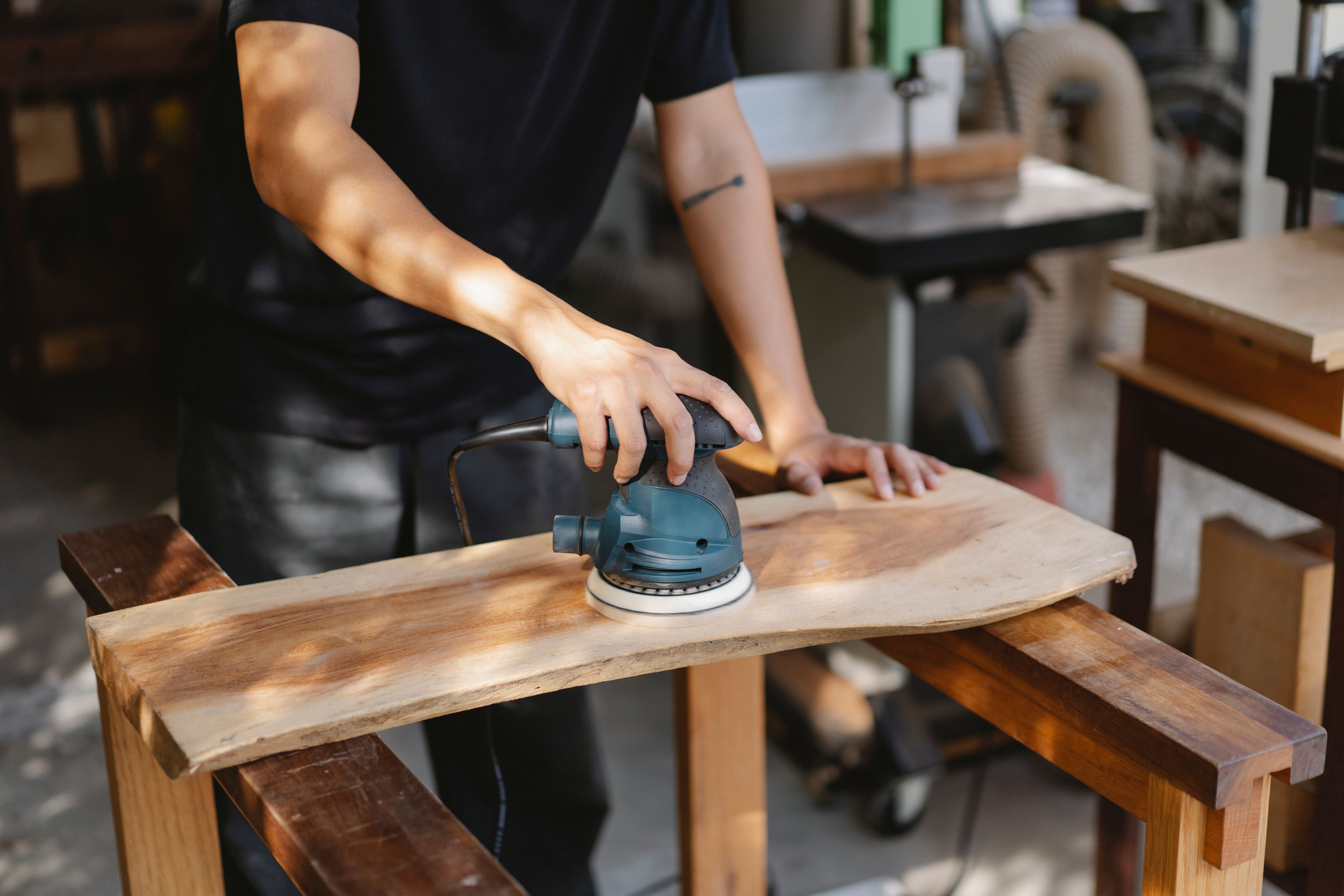 Craftsman using a hand sander to sand and polish a wooden plank during floor restoration