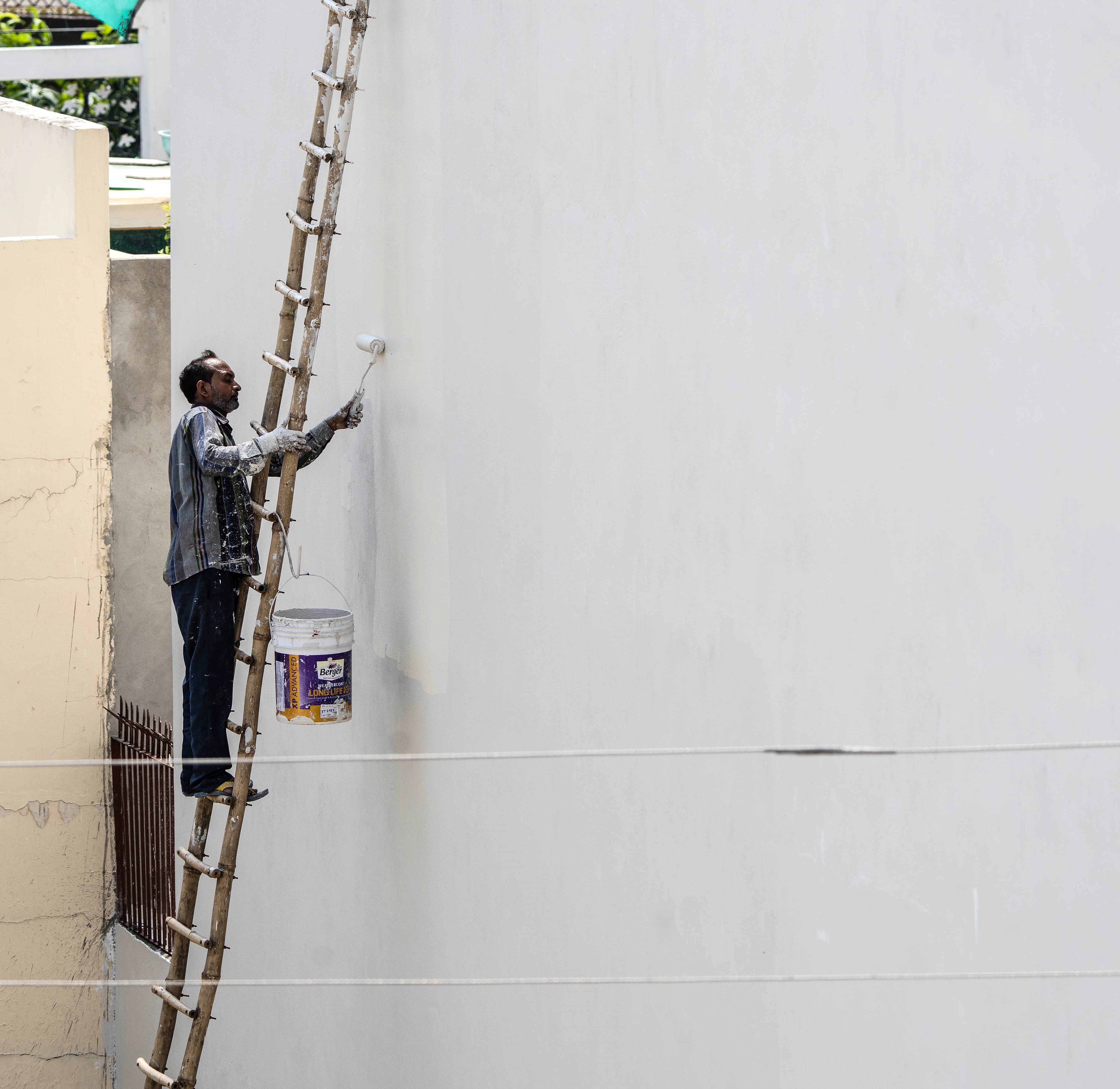 Painter on a ladder repainting a home exterior wall with a roller brush