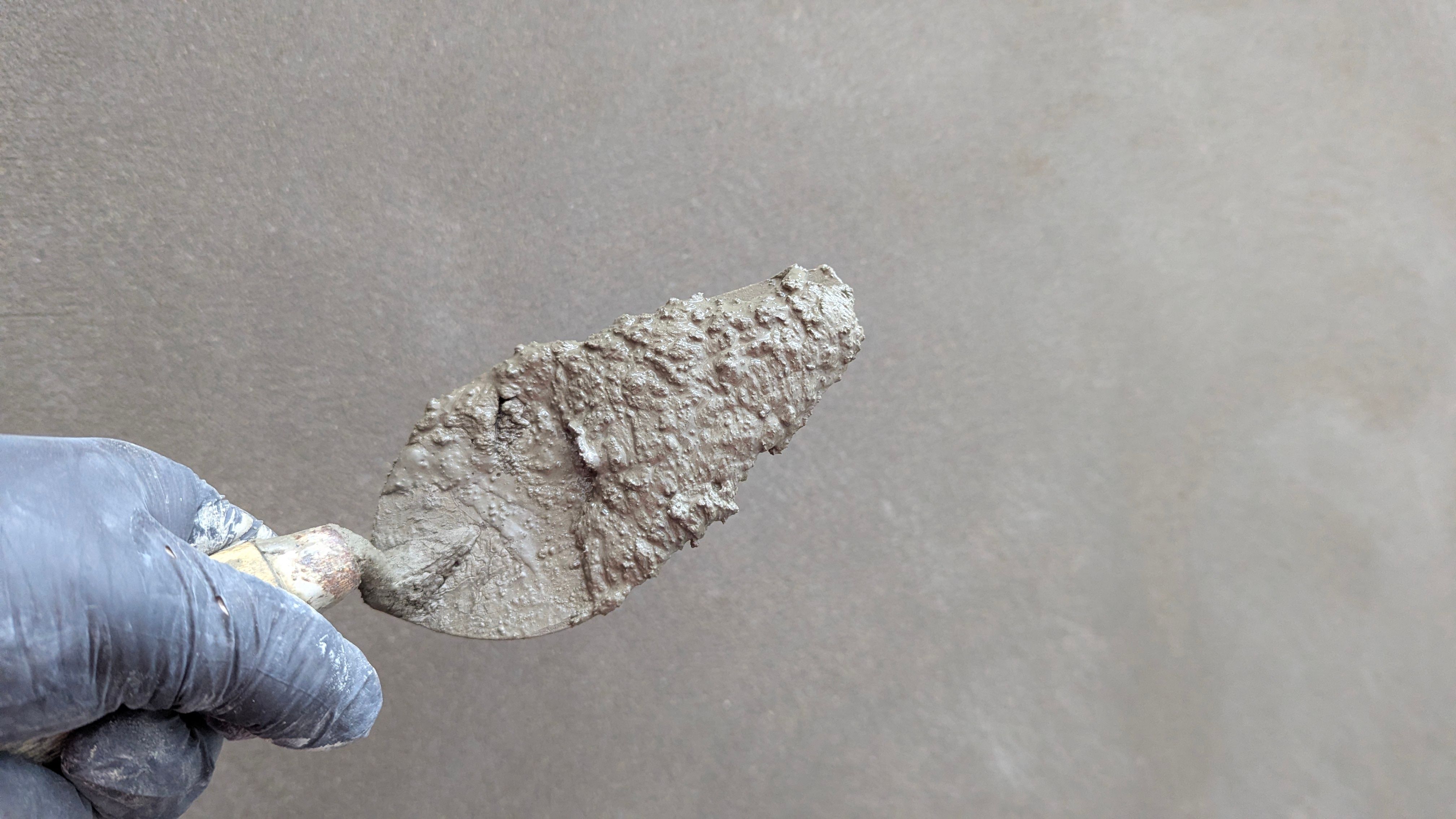Hand in a glove holding a plaster trowel against a smooth wall during repair work