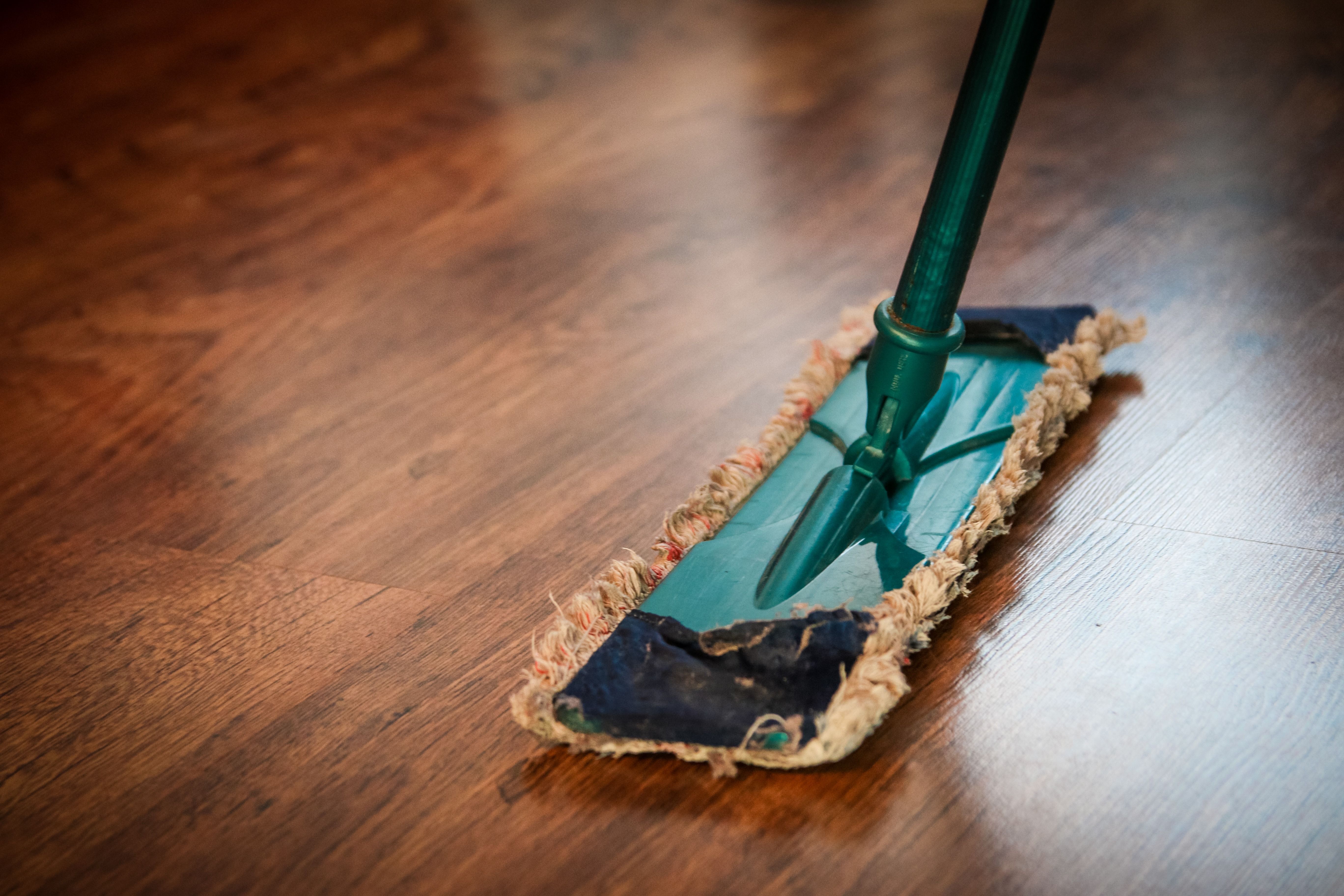 Person mopping and polishing a wooden floor to keep its refreshed finish looking clean and shiny