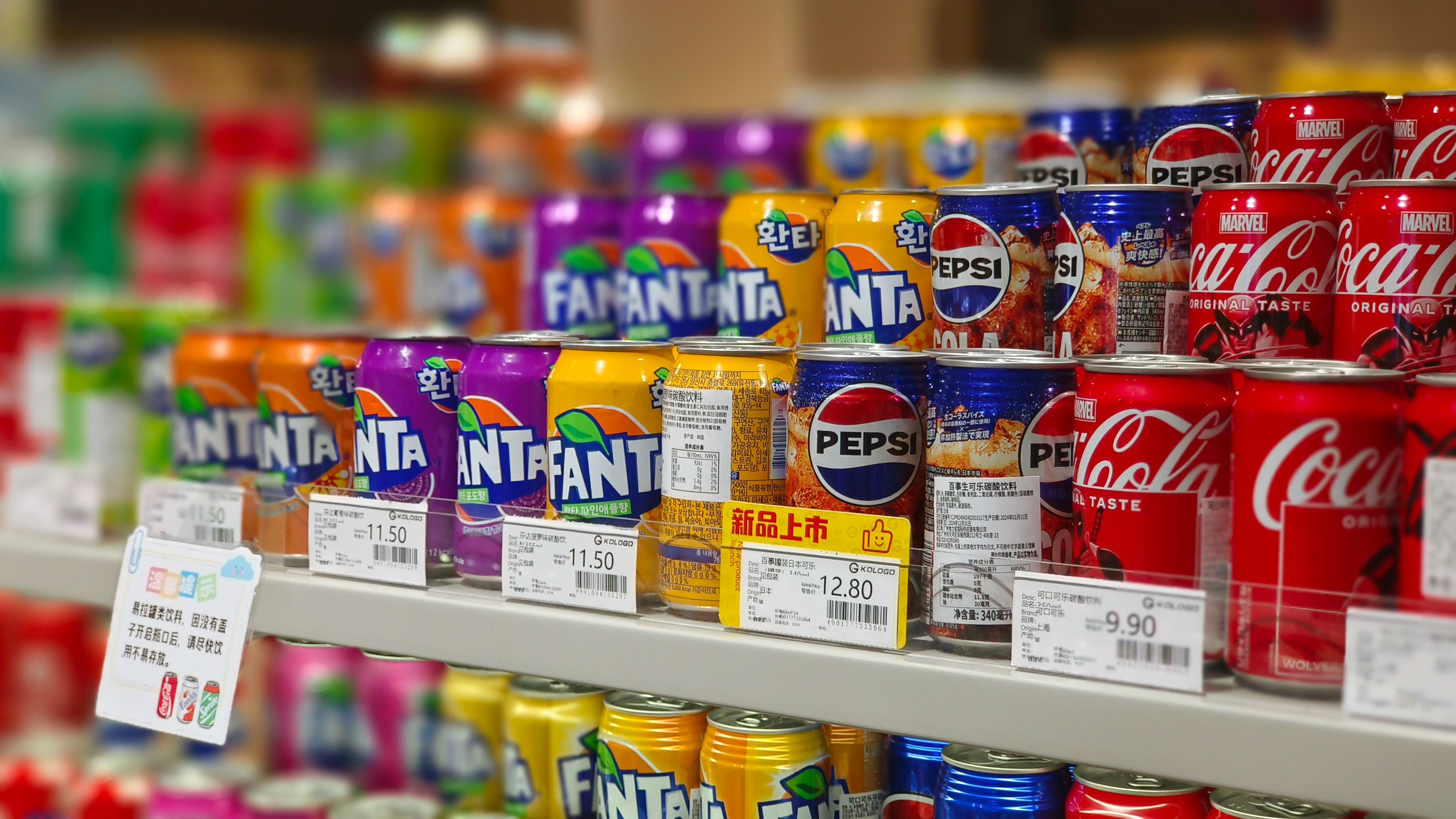 Colorful soda cans lined up on supermarket shelves with visible price tags