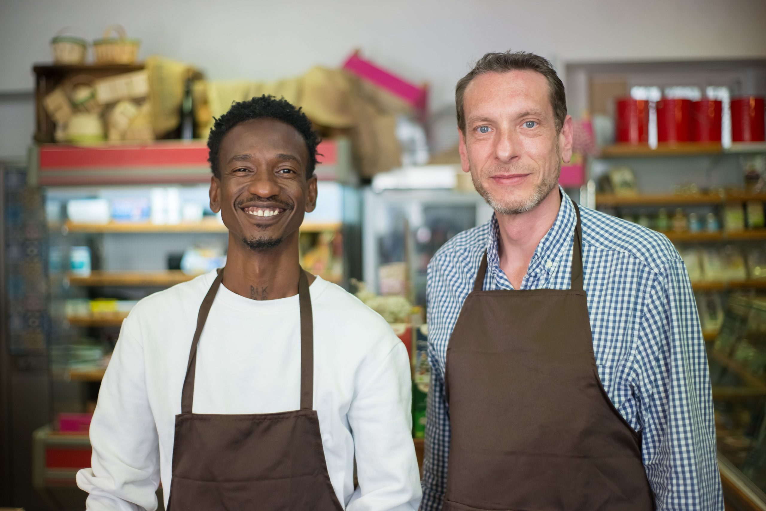 Two smiling small business store owners wearing aprons inside their shop