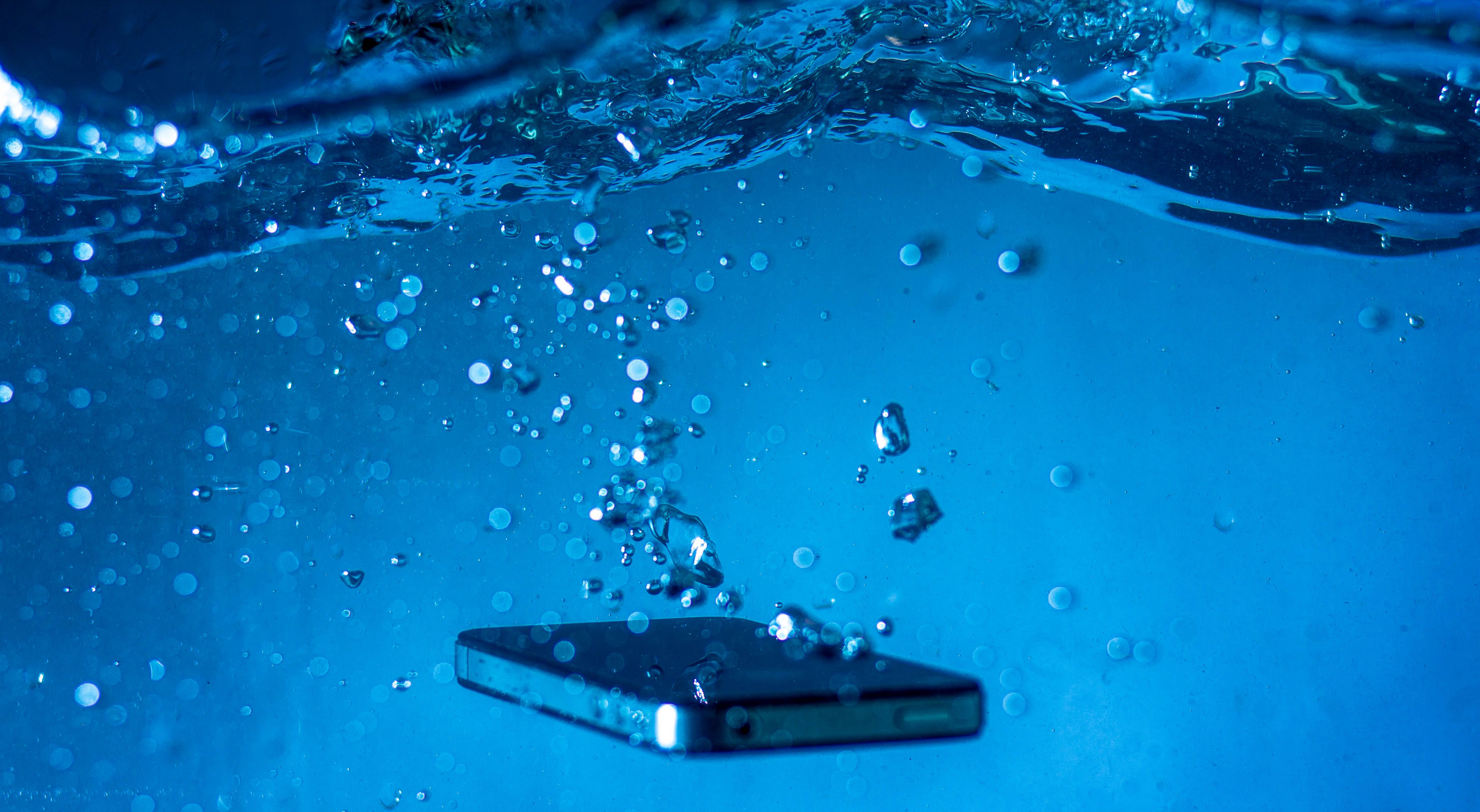 Smartphone submerged in water with bubbles, showing water damage that can wipe out photos and videos