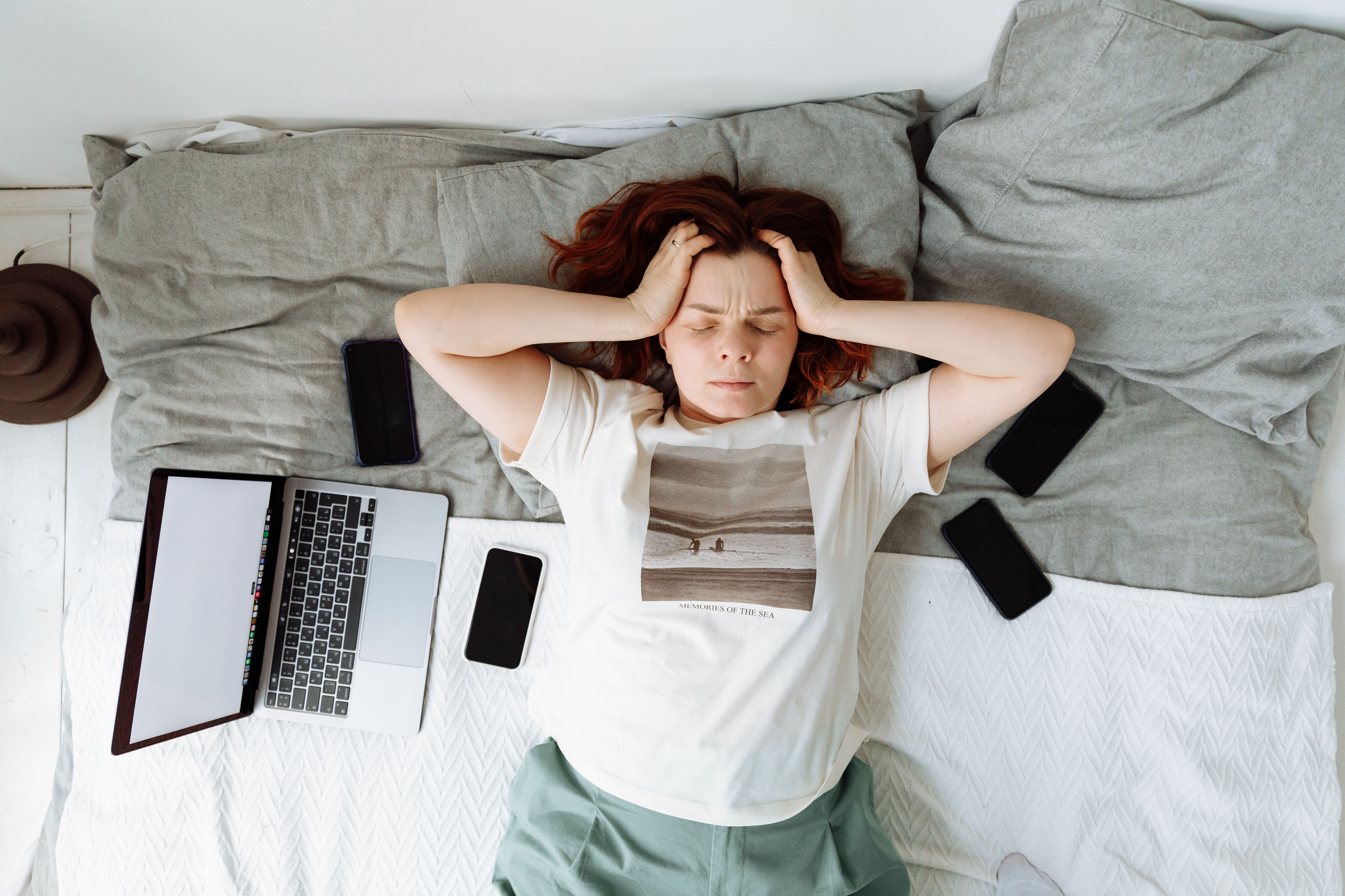 Distressed woman lying in bed surrounded by digital devices, stressed about losing phone photos and files