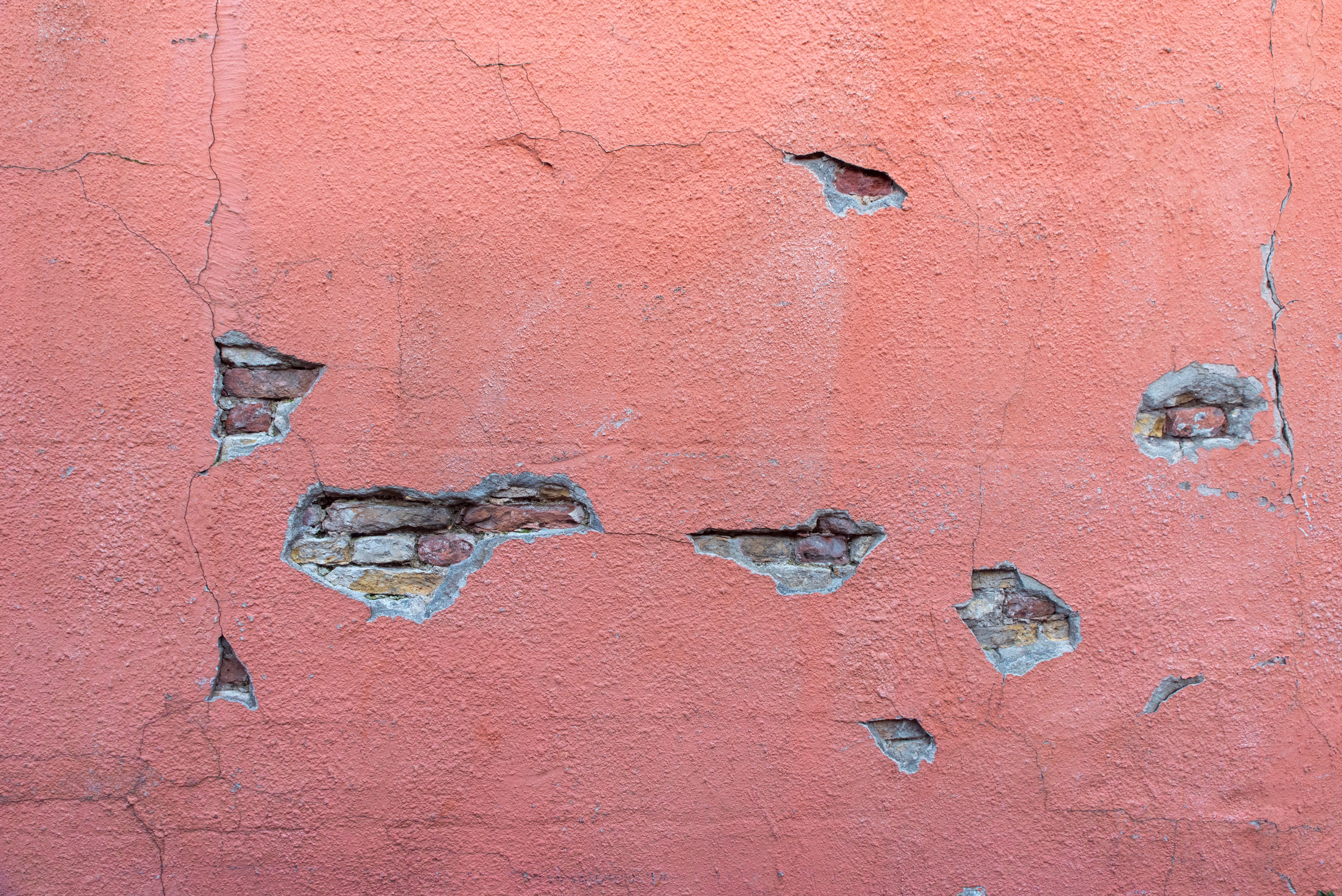 Cracked pink stucco exterior wall revealing the brick underneath