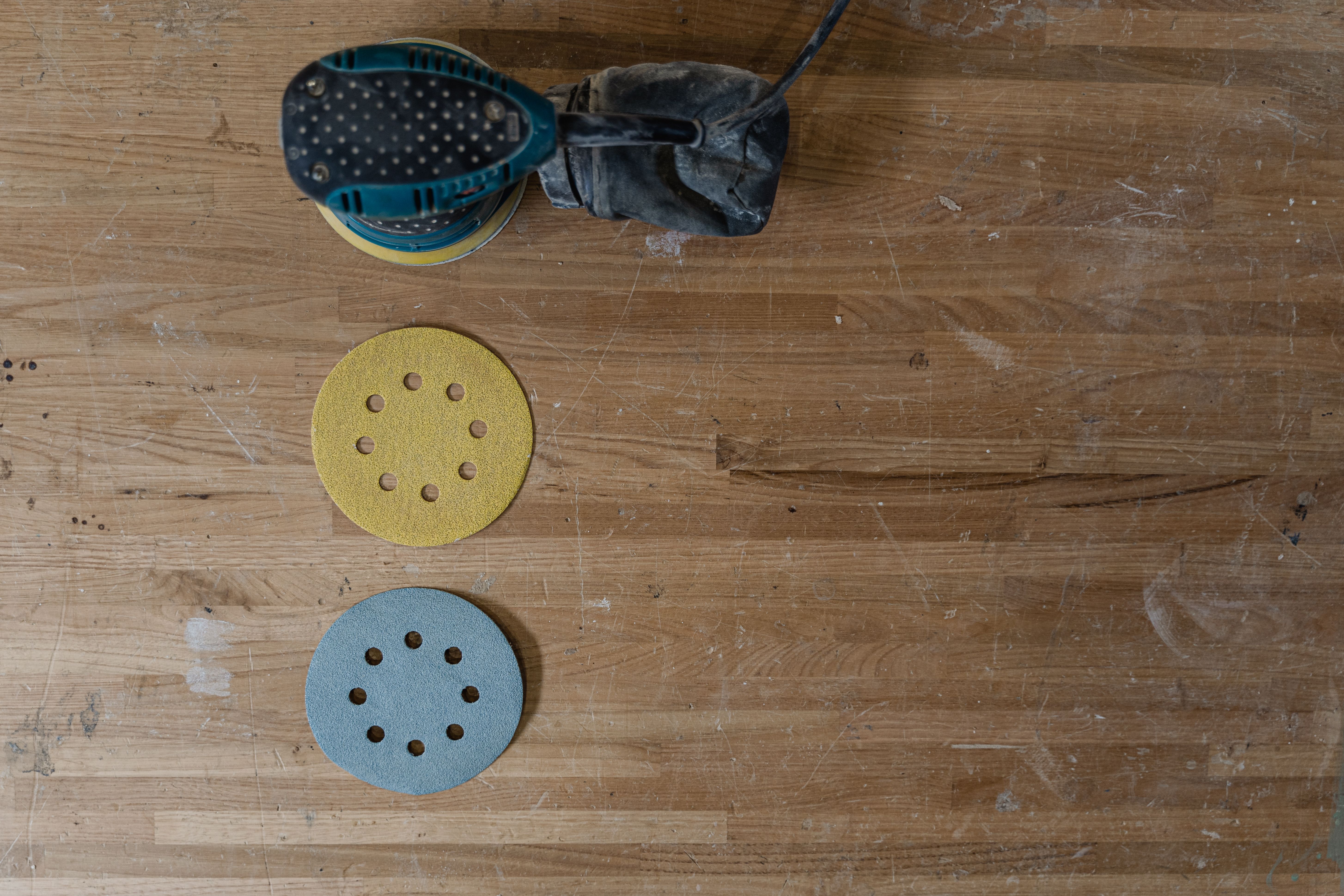 Electric floor sander with sandpaper discs on a wooden workshop table ready for sanding wood floors