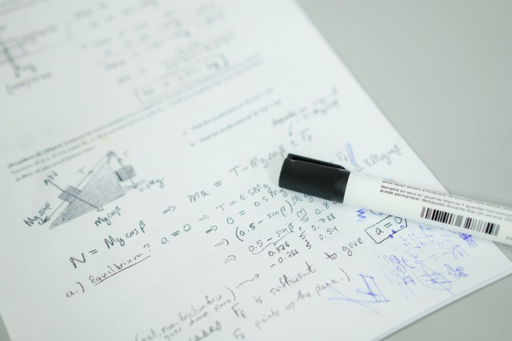 Mathematical formulas written on paper beside a marker for formula-based subject notes