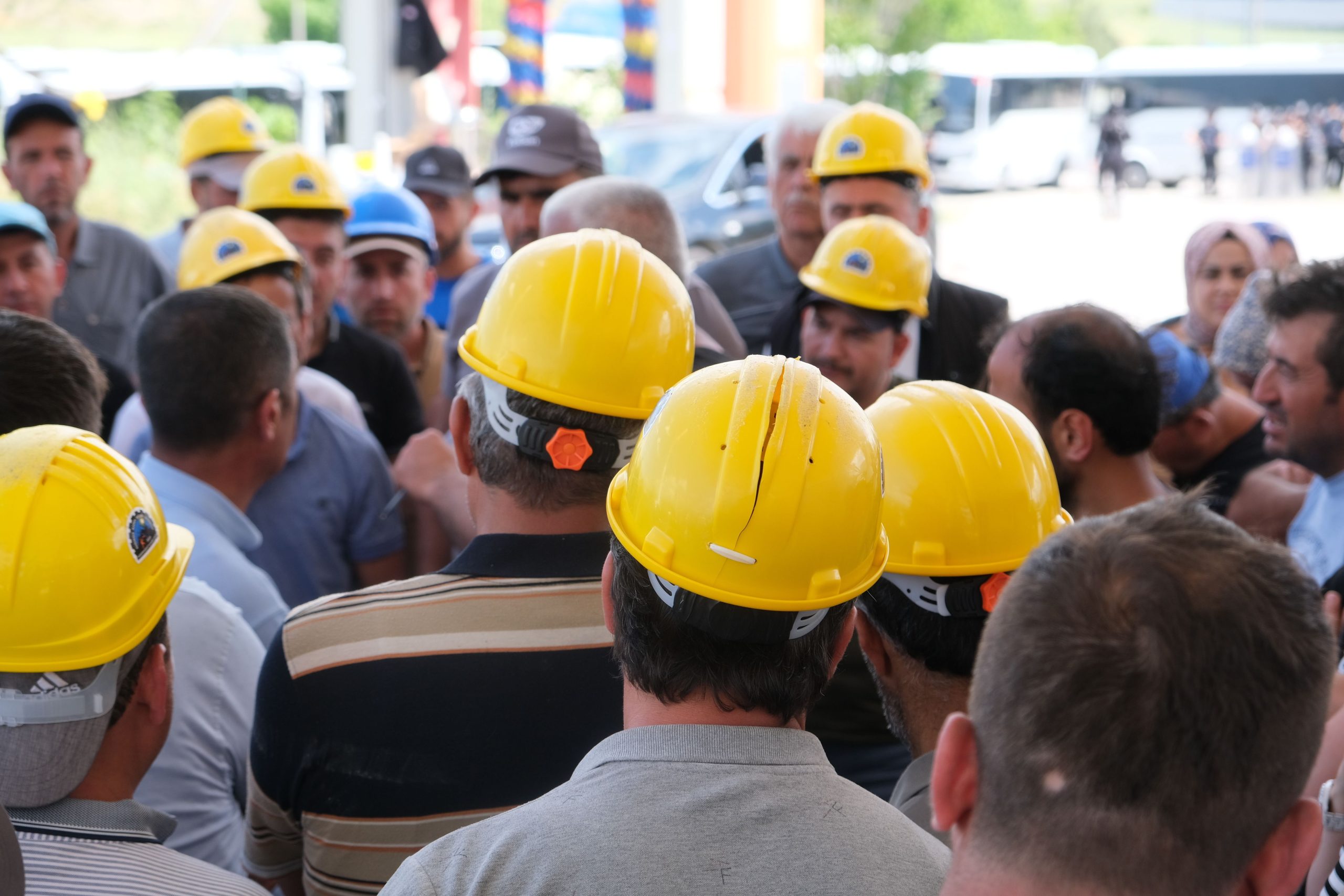 A gathering of construction workers wearing yellow hard hats, engaged in discussion outdoors.