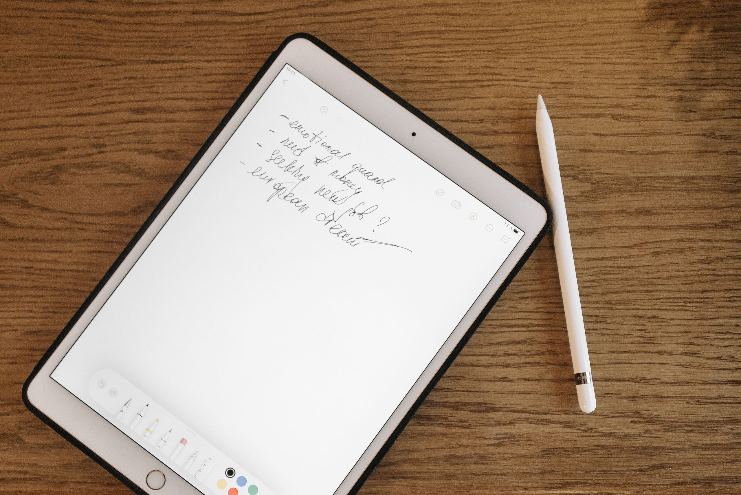 Tablet displaying handwritten digital notes beside a stylus on a wooden desk