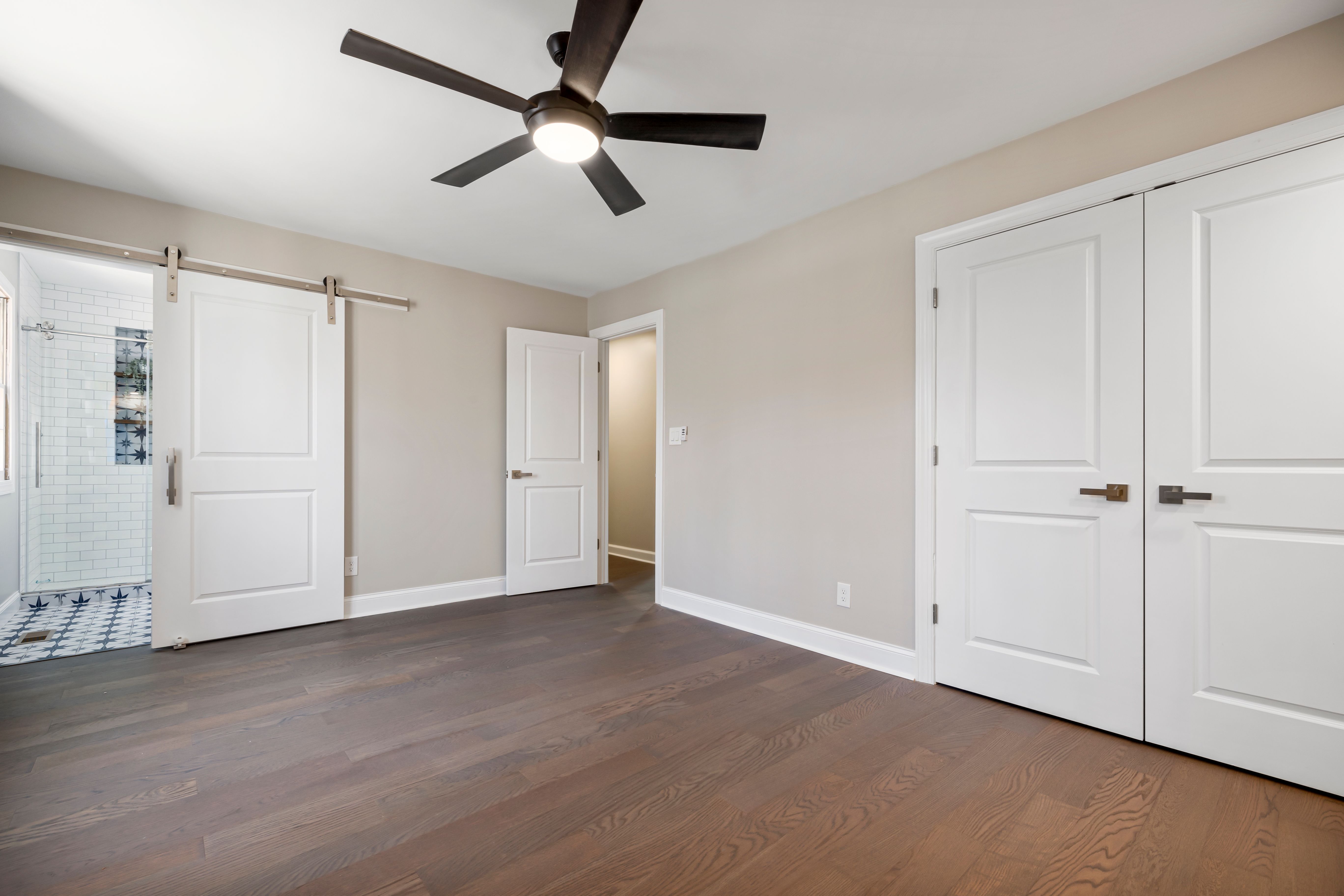Spacious empty room with wood floors, ceiling fan, and sliding barn door, suited to a guest room