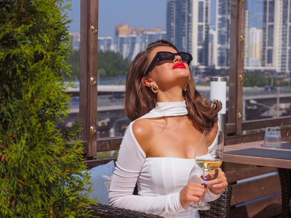 Confident woman in a white dress enjoying a drink on a city rooftop, evoking a polished, upscale dating lifestyle.