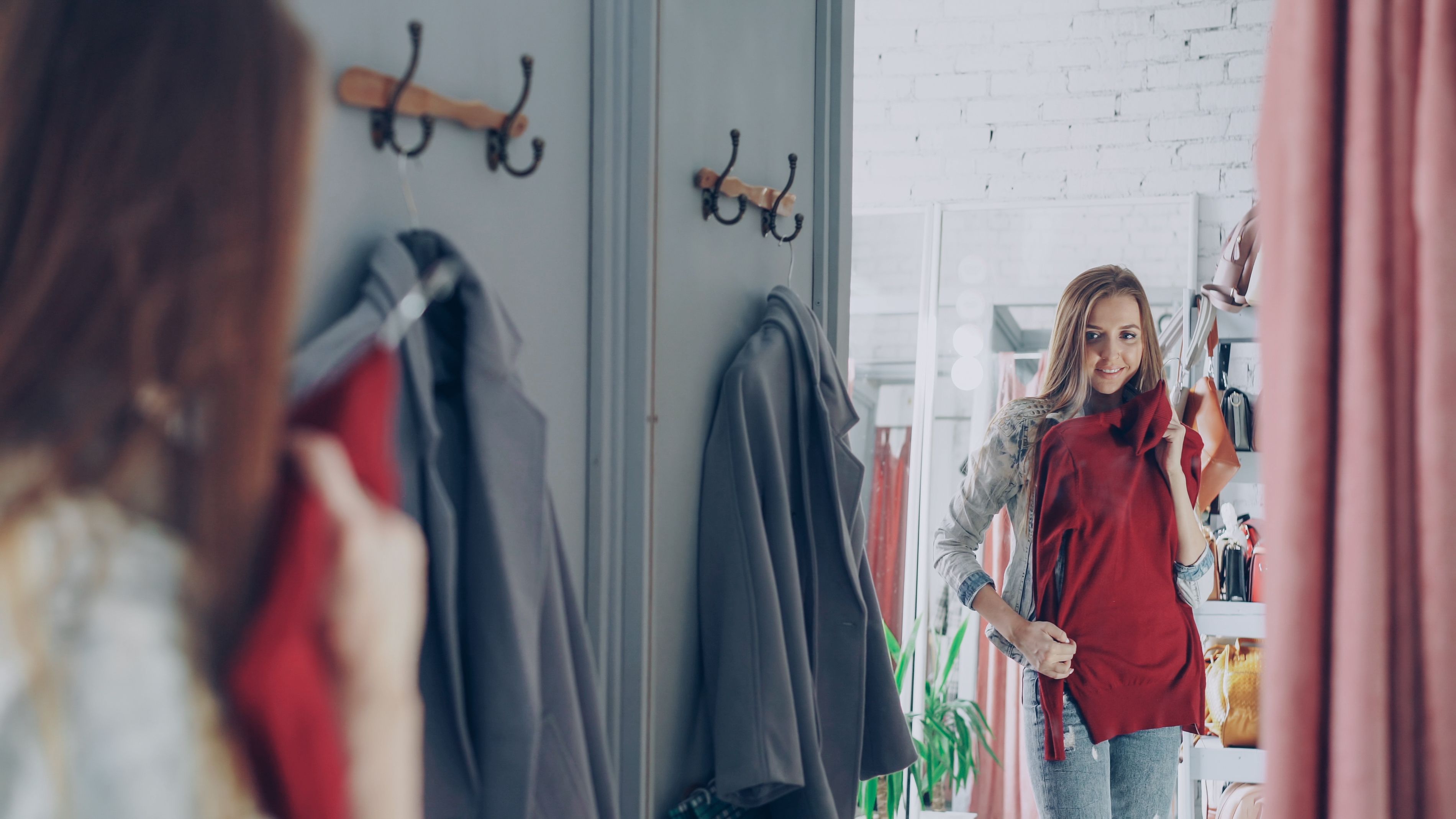 Smiling woman in a fashion boutique fitting room holding a red dress